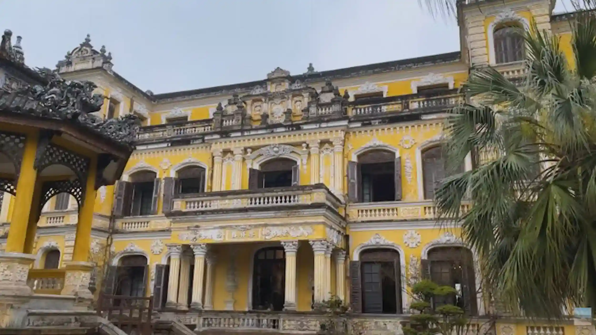 Yellow colonial palace with ornate balconies under gray skies during Hue's rainy season