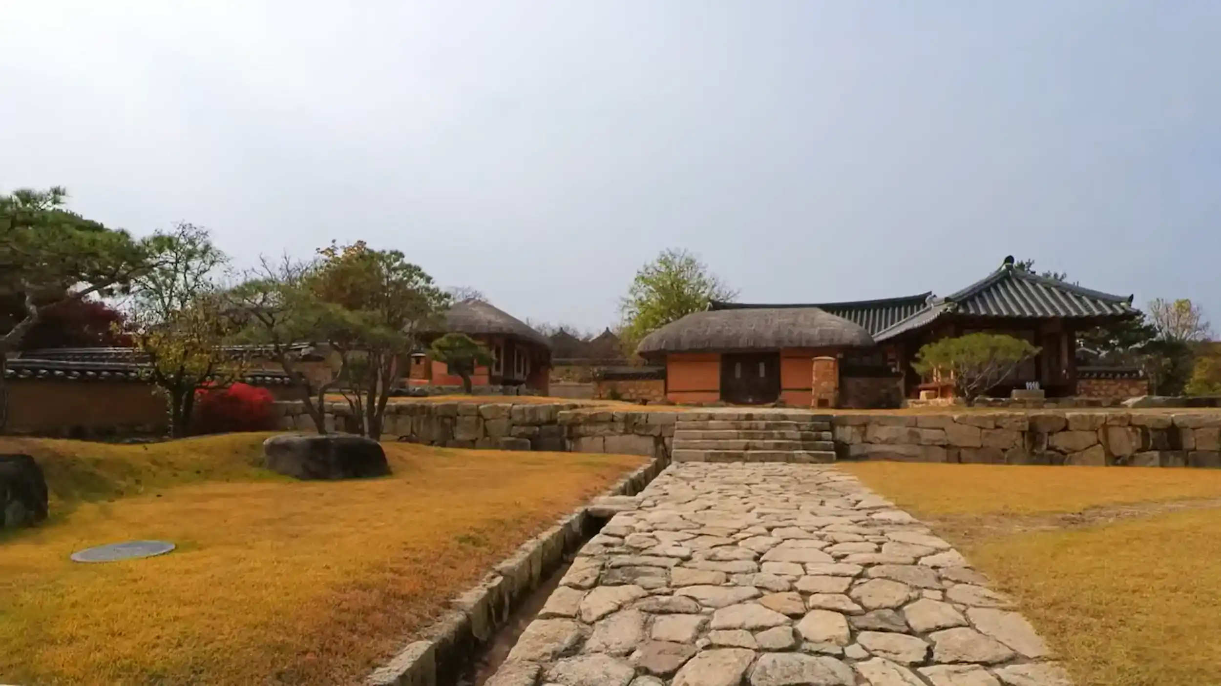 Andong Hahoe Village traditional Korean compound with thatched roof houses tile roofed buildings stone pathway walls and courtyard with autumn trees