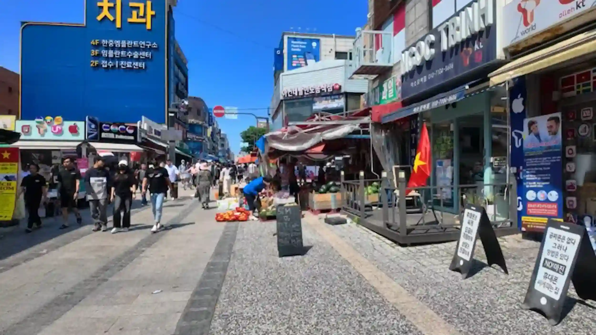 Bustling pedestrian street at Ansan markets with international shops, food vendors, and crowds on sunny day