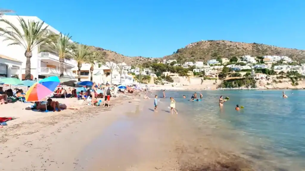 Moraira expensive Cala El Portet beach with swimmers and hillside villas backdrop.
