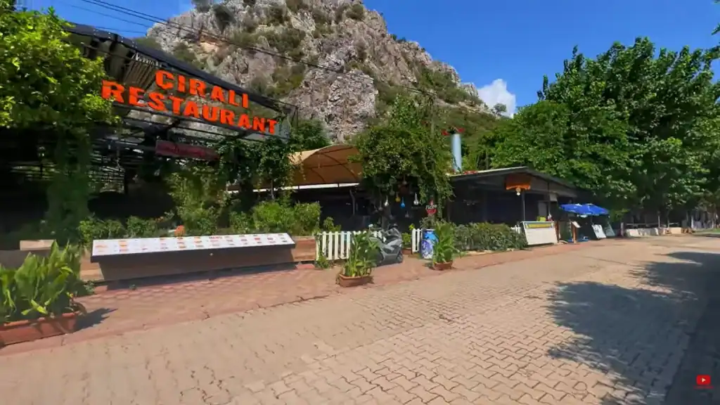 Çıralı restaurant with outdoor seating, shaded dining area, and dramatic limestone mountain backdrop in Turkey