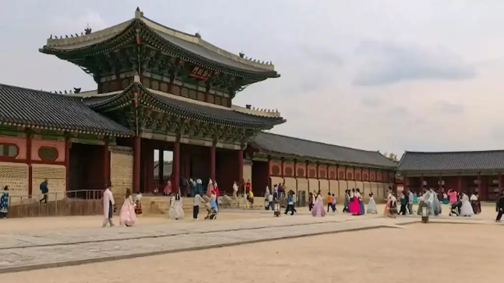 Gyeongbokgung Palace two story gate with green tile roof red pillars and visitors in colorful traditional hanbok clothing