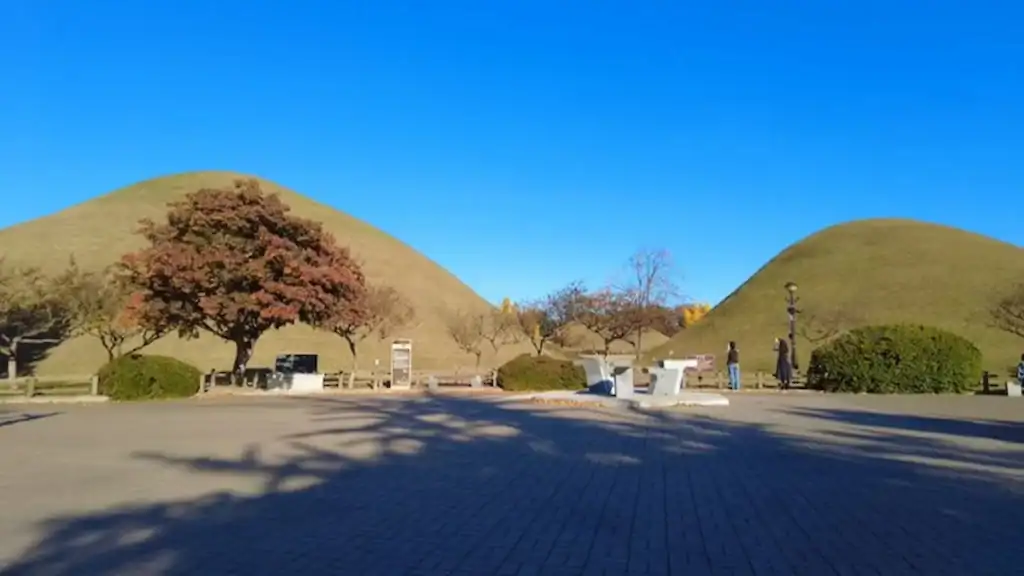 Ancient royal burial mounds in Gyeongju with grass covered tumuli autumn trees and blue sky
