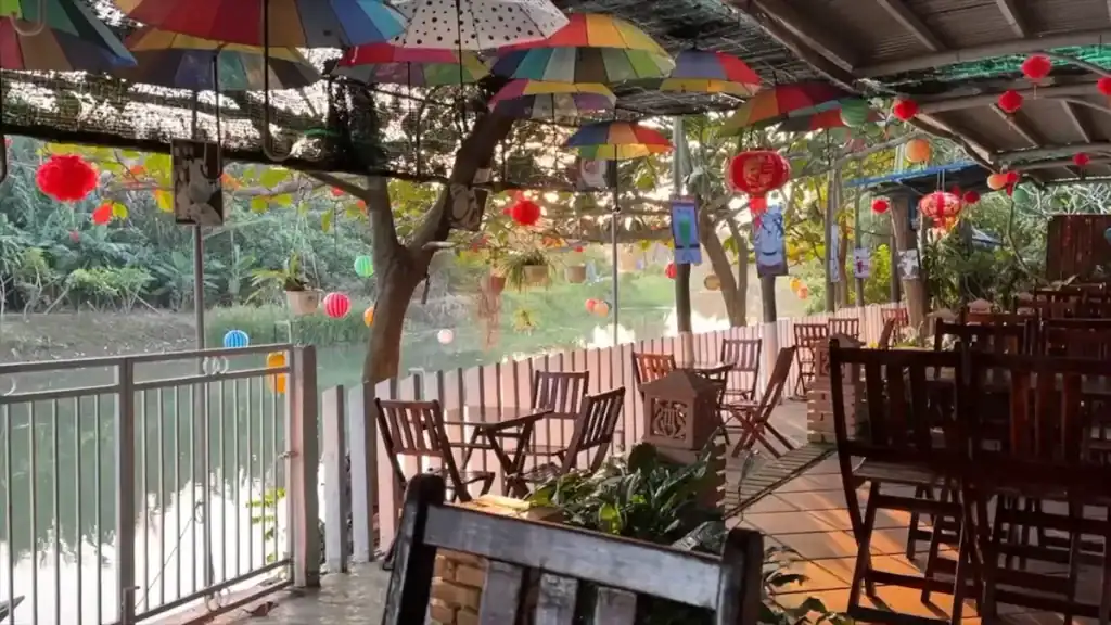 Restaurant with colorful umbrellas lanterns and wooden tables overlooking tranquil green waterway