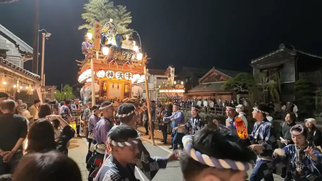 Illuminated multi-tiered festival float surrounded by dancers in traditional clothing at Sawara Grand Festival