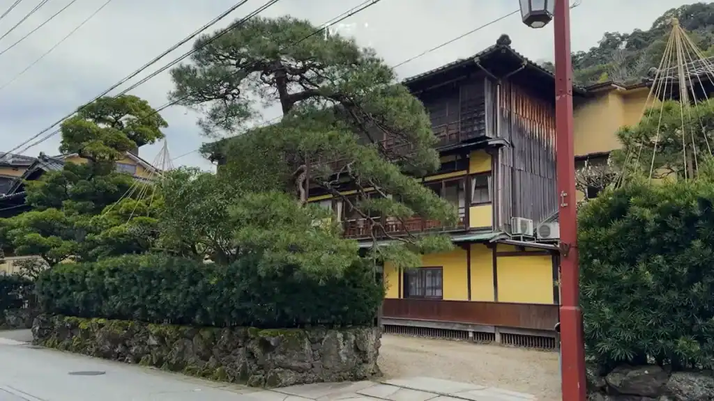 Kinosaki Budget Ryokans - Mikiya's traditional yellow and dark wood exterior with mature pine trees