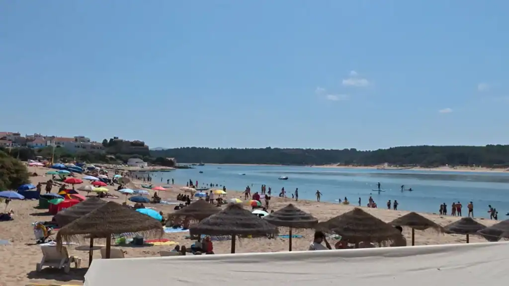 Busy town beach with colorful umbrellas at Milfontes how many days to relax
