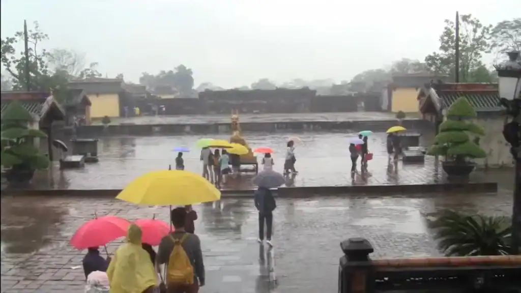 Tourists with colorful umbrellas walking through wet plaza during Hue's rainy season