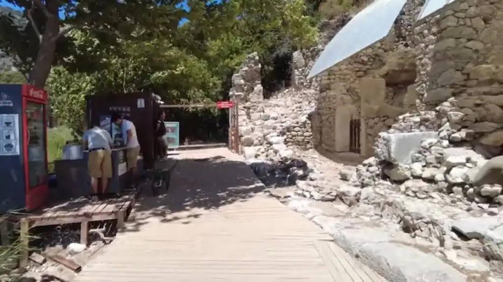Olympos beach access pathway through ancient ruins with wooden boardwalk, ticket booth, and historic stone structures