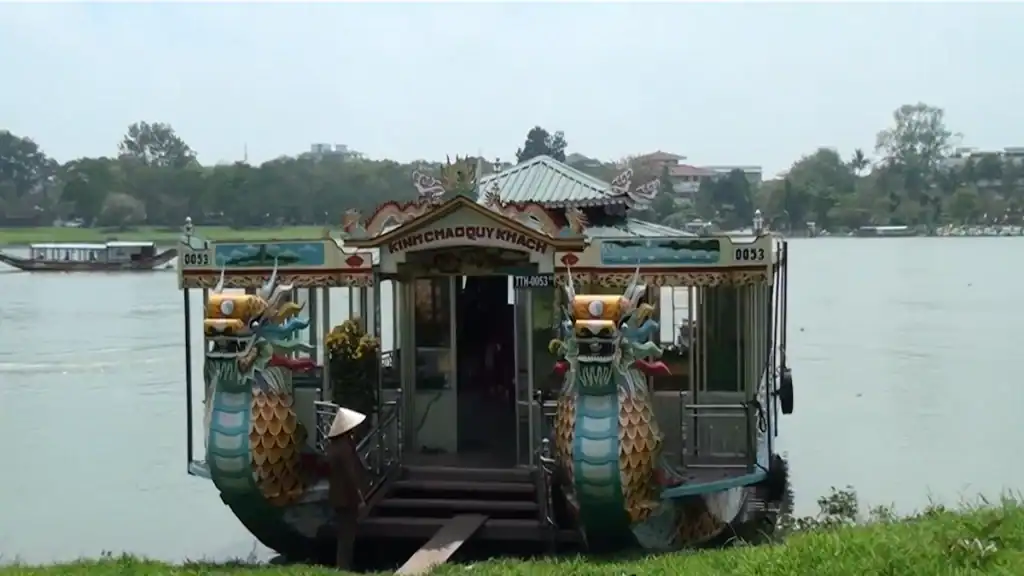 Dragon-decorated tour boat moored along riverbank during Hue's rainy season