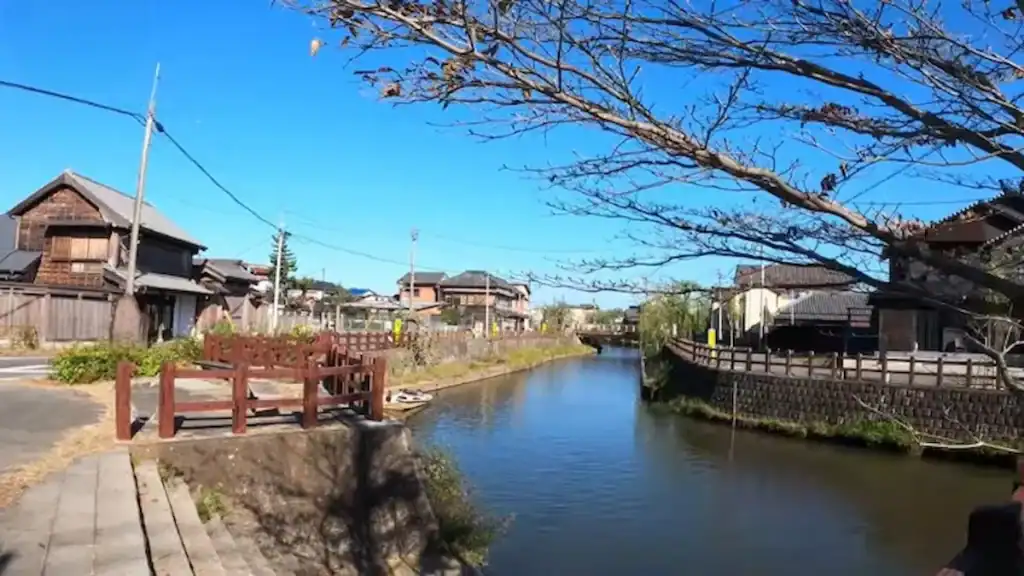 Sawara canal with traditional wooden bridge, bare winter trees, and historic buildings along the waterway. Comparing Sawara vs Kawagoe