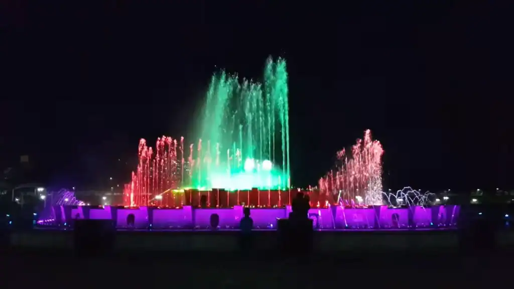 Nighttime water fountain show with colorful illuminated jets in green red purple creating spectacular display