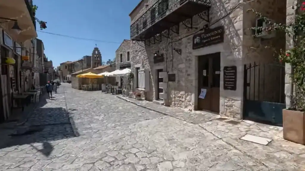 Cobblestone street running through Areopoli's old quarter, flanked by rough-cut stone buildings and a taverna with outdoor seating under yellow and white umbrellas