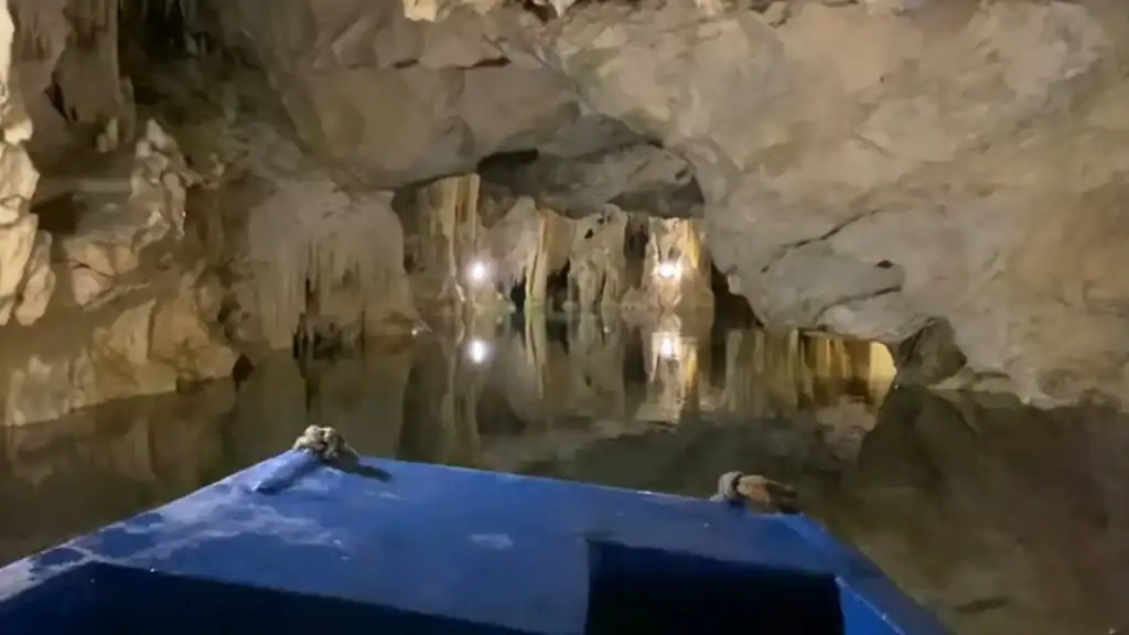 Blue boat bow on still underground water inside the Diros Caves Mani Peninsula, stalactites hanging from limestone ceiling with installed lights reflecting on the surface