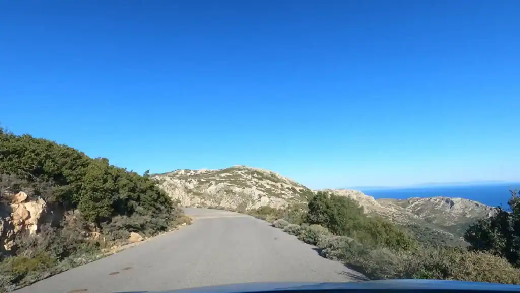 Narrow unmarked road climbing through rocky scrubland near Lagia, sea visible to the right between limestone ridges