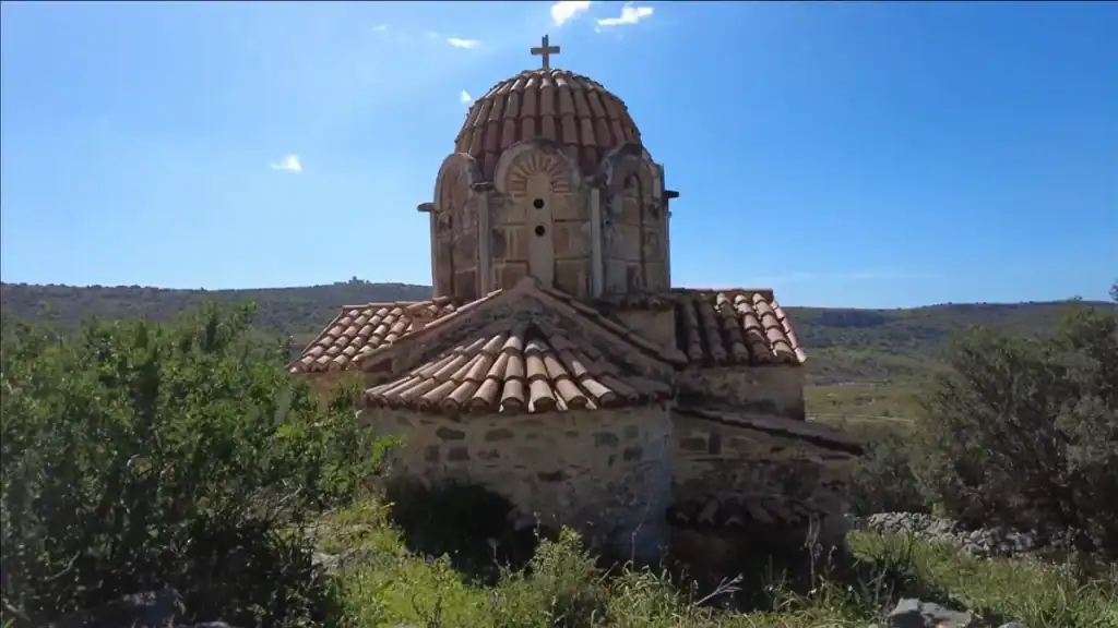 Byzantine church at Episkopi with a tiled dome topped by a cross, rising above scrubland and low hills under a clear blue sky
