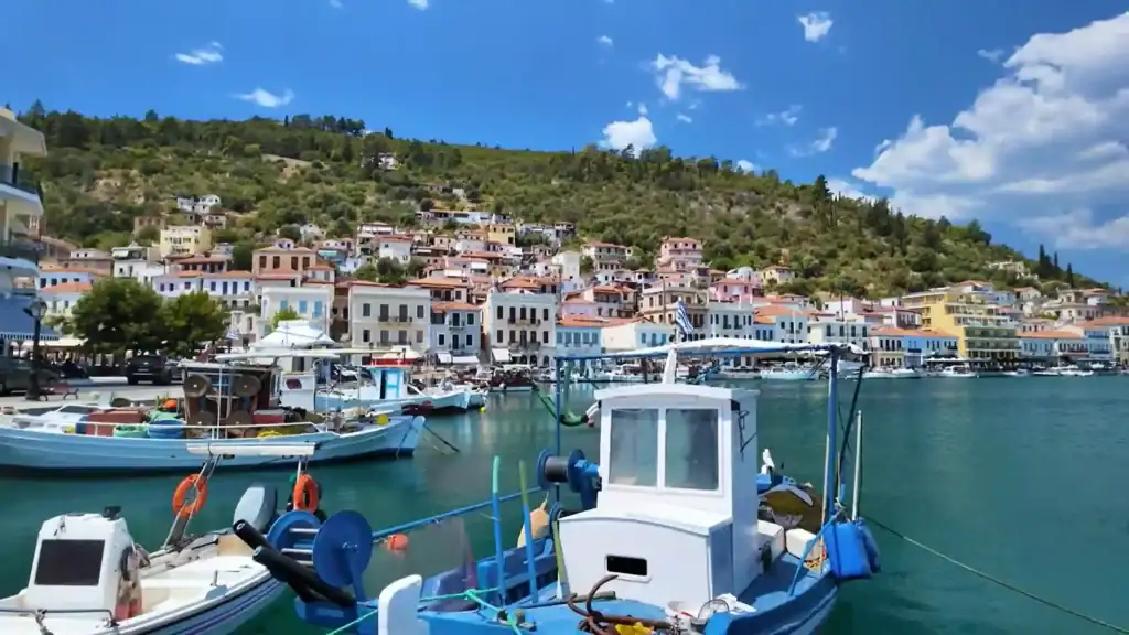 Fishing boats moored in Gytheio harbour with pastel-fronted waterfront buildings and a densely wooded hill rising behind them