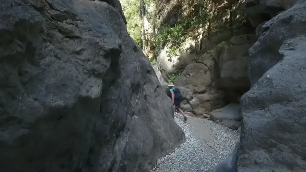 Viros Gorge Kardamyli hiker navigating narrow rocky passage between towering walls.