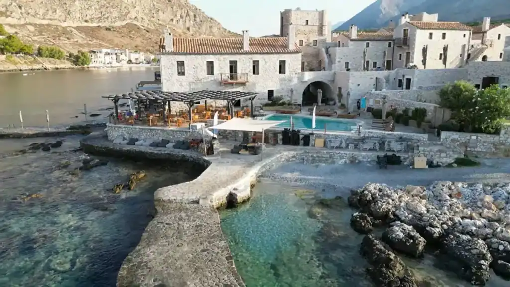 Small harbour at Gerolimenas with turquoise water, a handful of moored boats, and stone buildings clustered along the shoreline beneath bare limestone cliffs