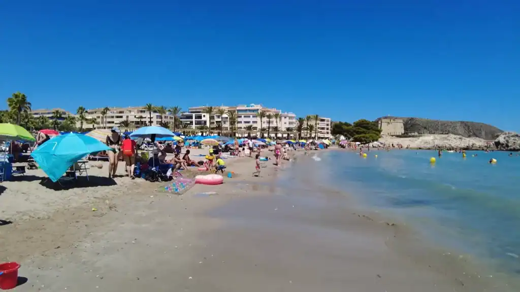 Busy L'Ampolla crowded with beachgoers and umbrellas.
