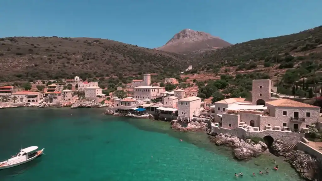 Turquoise harbour at Limeni with stone tower houses clustered at the waterline and a bare-peaked mountain rising behind the village