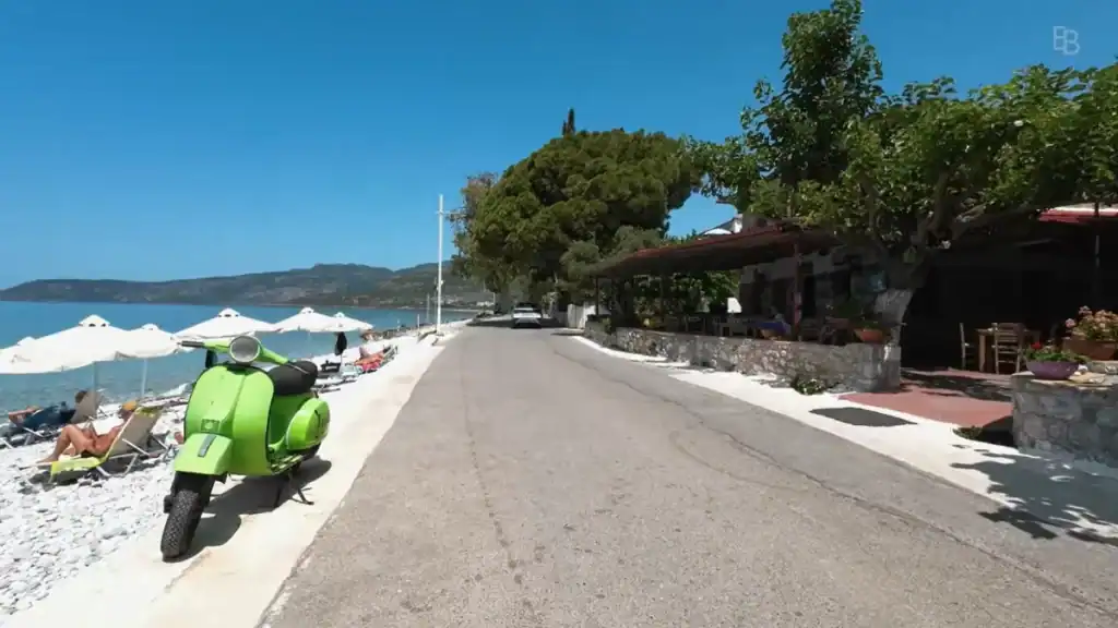 Kardamyli Beach with green scooter parked outside beachfront taverna in sunshine.