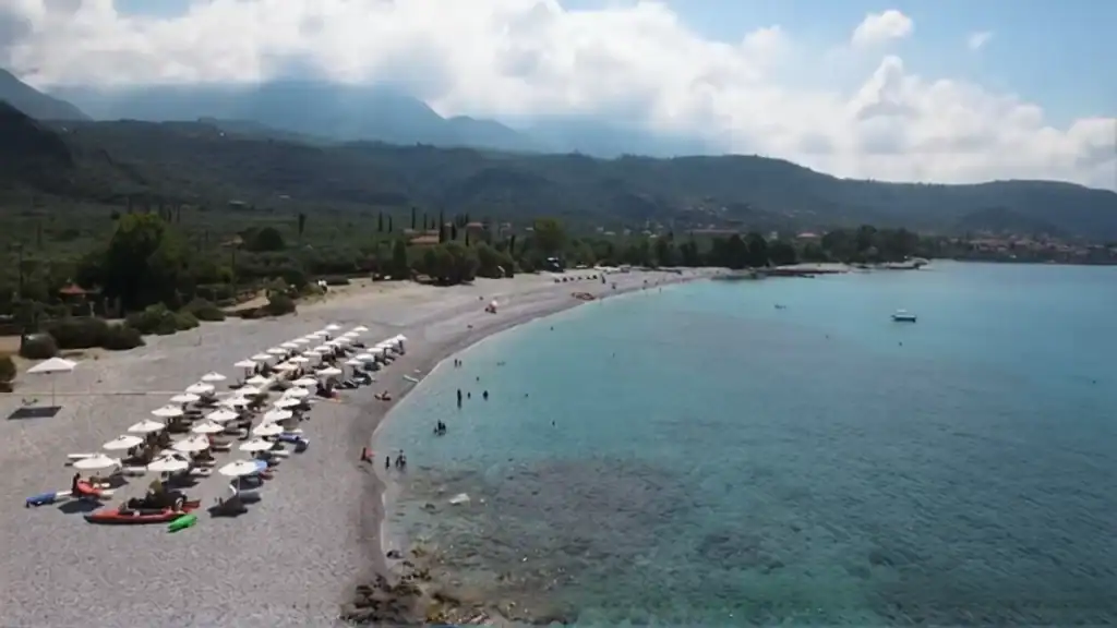 Kardamyli Beach with white umbrellas and sunbeds along the pebble shore.