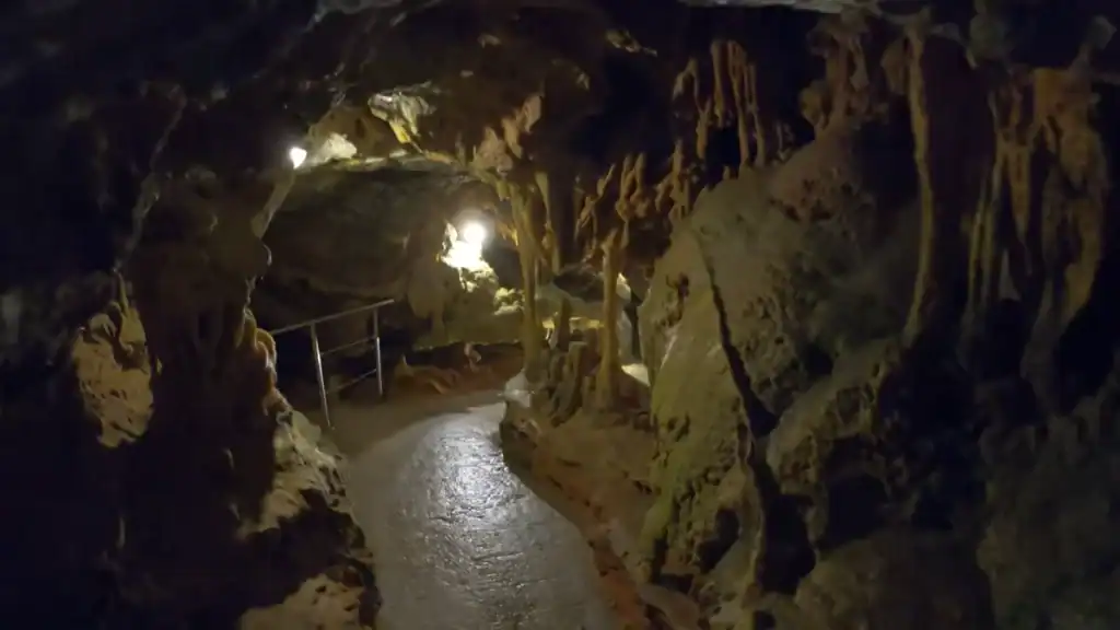 Narrow paved walkway curving through stalactite-filled chambers at Diros Caves Mani Peninsula, lit by small installed spotlights receding into darkness