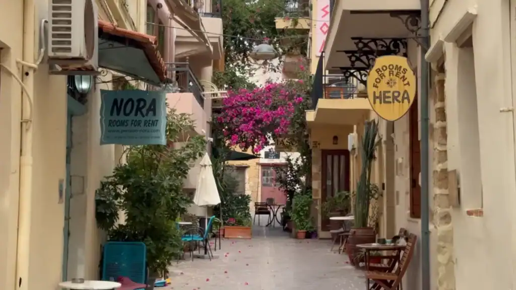 Quiet alleyway with rooms-for-rent signs and vivid pink bougainvillea overhead, part of walking in Chania old town