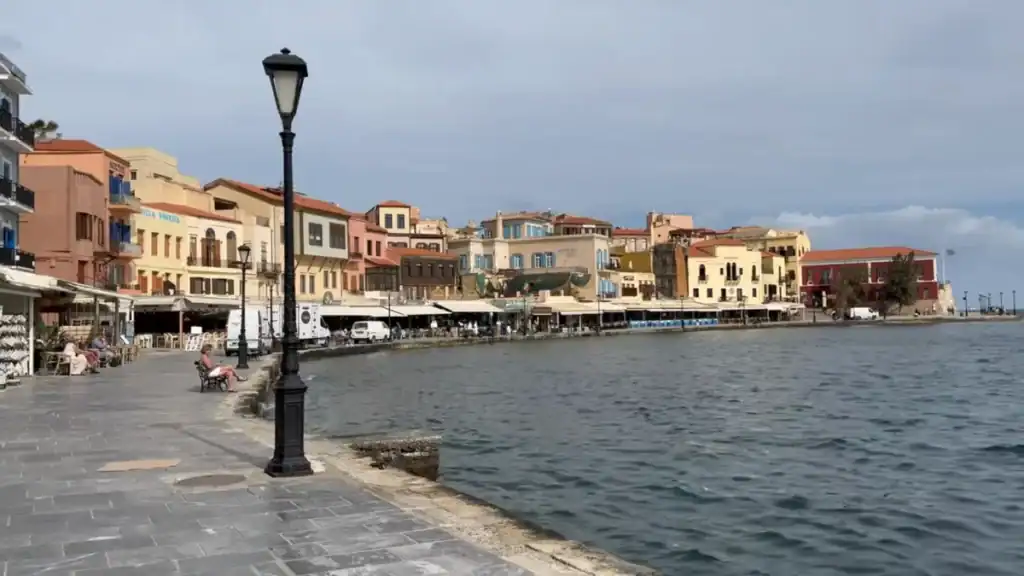 Quiet waterfront promenade in Chania in November, a cast-iron lamp post in the foreground and colourful Venetian-era buildings lining the far quay