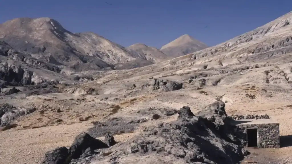 Bare limestone terrain in the White Mountains of Chania, a small stone shelter set among dark volcanic rock with pale peaks behind