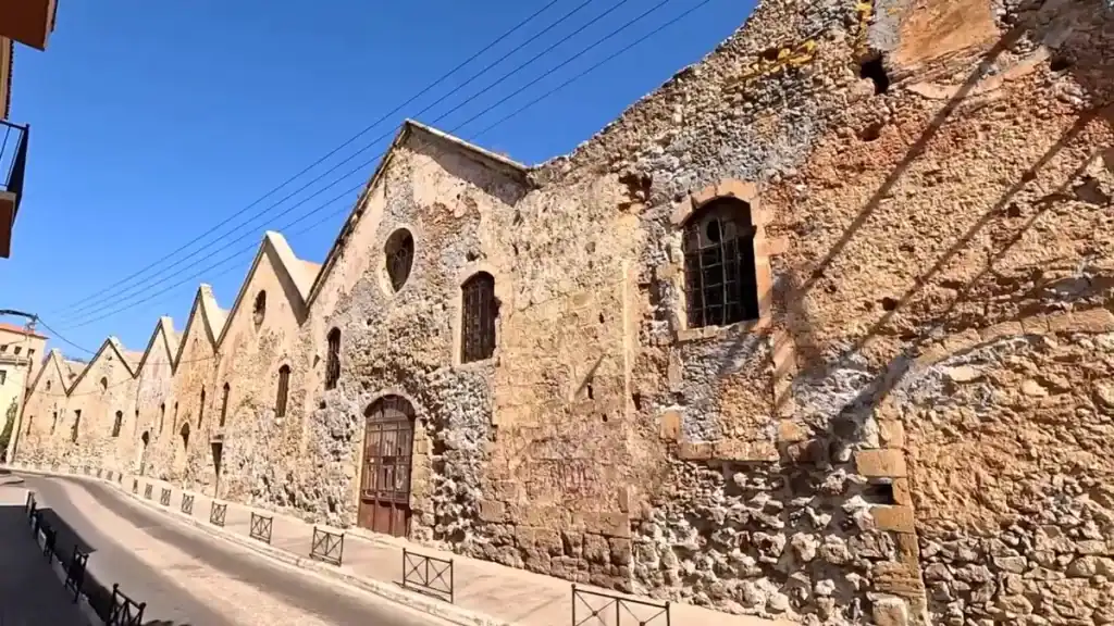 Venetian shipyard walls in Chania, weathered stone facades with arched windows and gabled roofline running along a quiet street