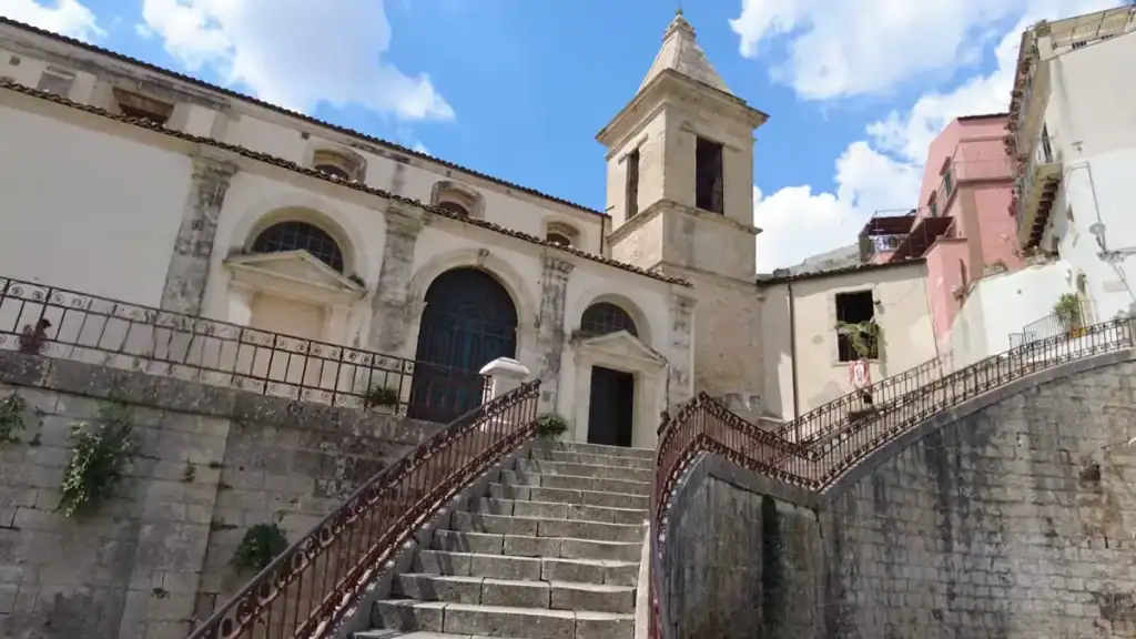 Chiesa di Santa Maria delle Scale seen from street level, its broad staircase splitting around a central arch, bell tower rising behind the facade against a blue sky