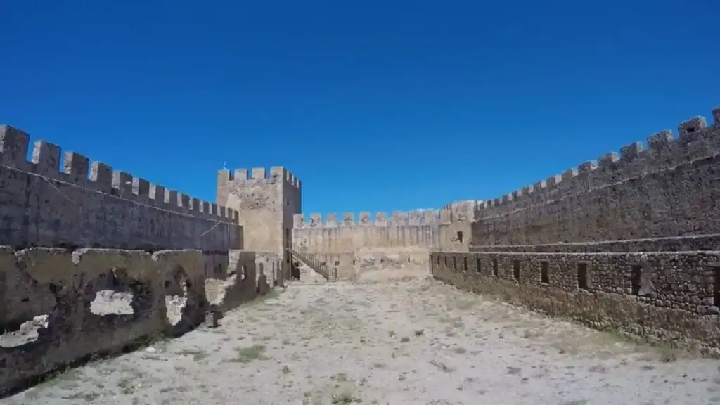 Interior courtyard of Frangokastello castle, crenellated walls running the full length on both sides toward a central keep under deep blue sky