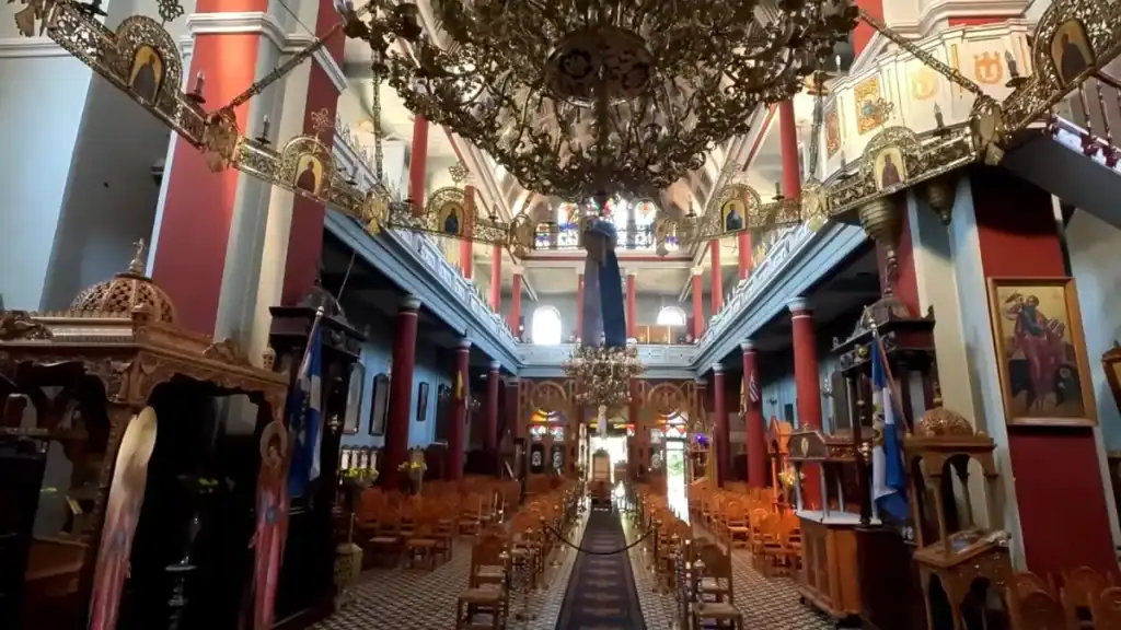 Ornate interior of the Church of St Nicholas in Chania, elaborate brass chandeliers hanging above rows of wooden chairs and icon-lined galleries