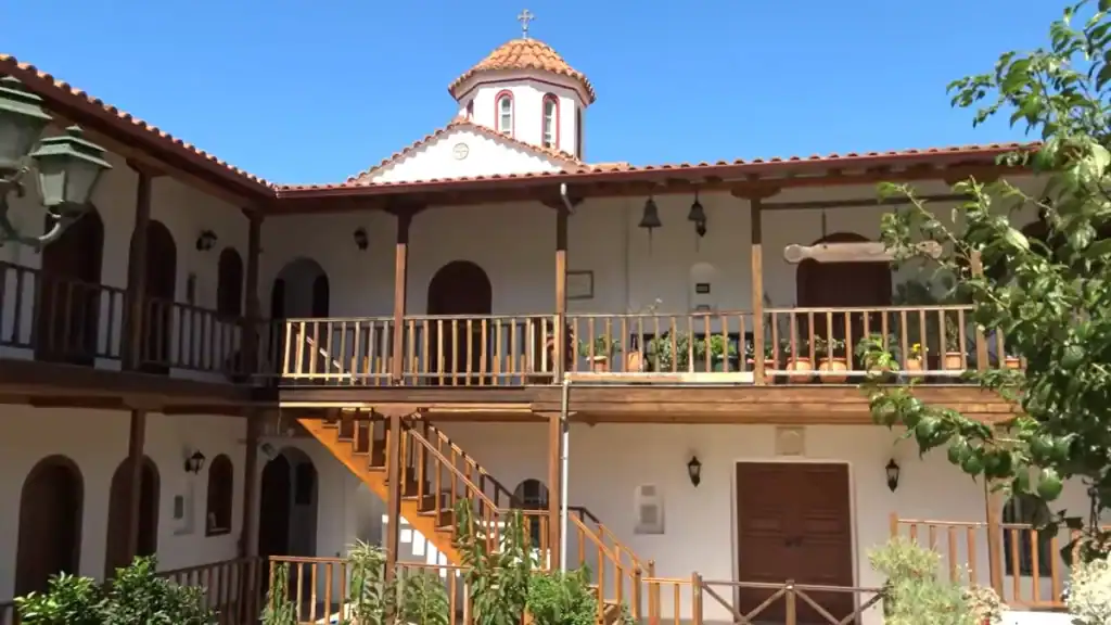 Faneromeni Monastery courtyard in Lefkada in September, its whitewashed two-storey facade with wooden balconies and terracotta-domed chapel rising against a deep blue sky