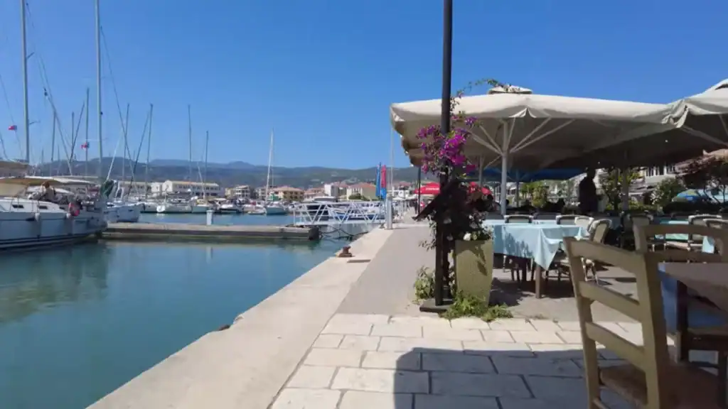 Waterfront taverna tables beside the marina in Lefkada Town, sailing boats moored along the quay and the town's low rooftops visible across the water