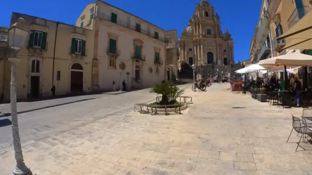 Piazza del Duomo in Ragusa Ibla, with the ornate facade of the Duomo di San Giorgio closing the square and café tables set out to the right - the kind of stop any Ragusa travel guide would place near the top of the list.