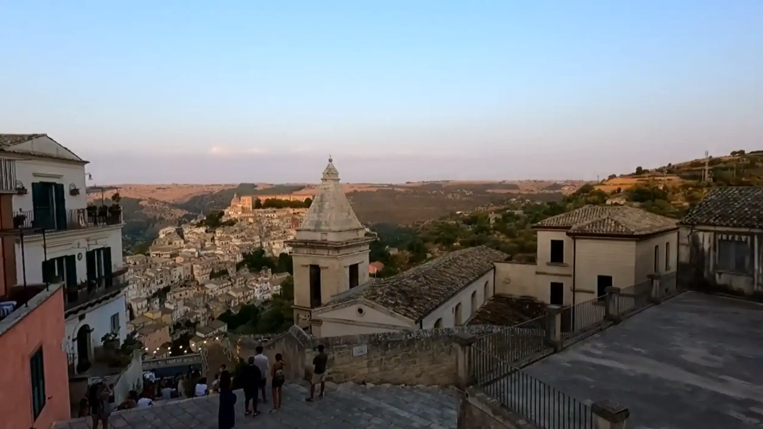 Settling into Ragusa at dusk, with the bell tower of Santa Maria delle Scale in the foreground and Ragusa Ibla's baroque rooftops cascading down into the valley below