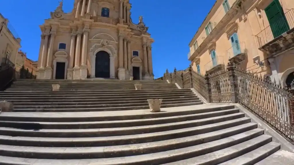 Wide stone steps lead up to the Cathedral of San Giorgio, its tiered baroque facade ornate with columns and sculpted detail - central to Ragusa Ibla travel and the UNESCO-listed lower town