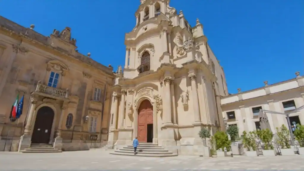 Chiesa di San Giuseppe's ornate baroque facade rising steeply above a lone figure climbing its entrance steps, flanked by the Palazzo della Cancelleria on the left and café seating to the right
