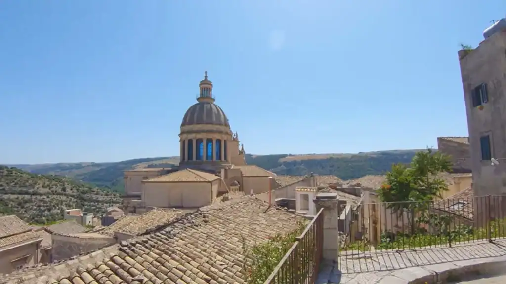 The dome of the Cathedral of San Giorgio rising above terracotta rooftops in Ragusa Ibla, a destination worth driving to Ragusa to see, with hills stretching behind it.