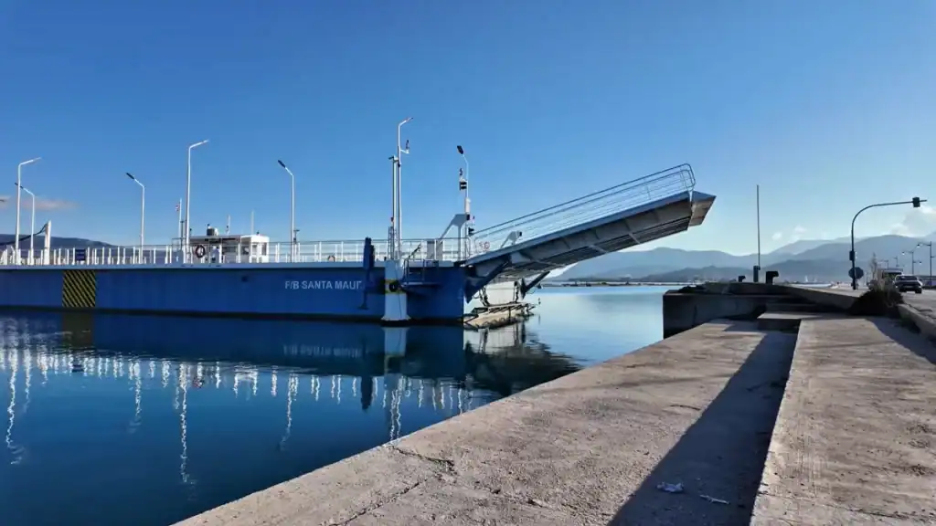 The F/B Santa Maura ferry moored at the swing bridge crossing that connects Lefkada island to the Greek mainland, its ramp raised against a clear blue sky.