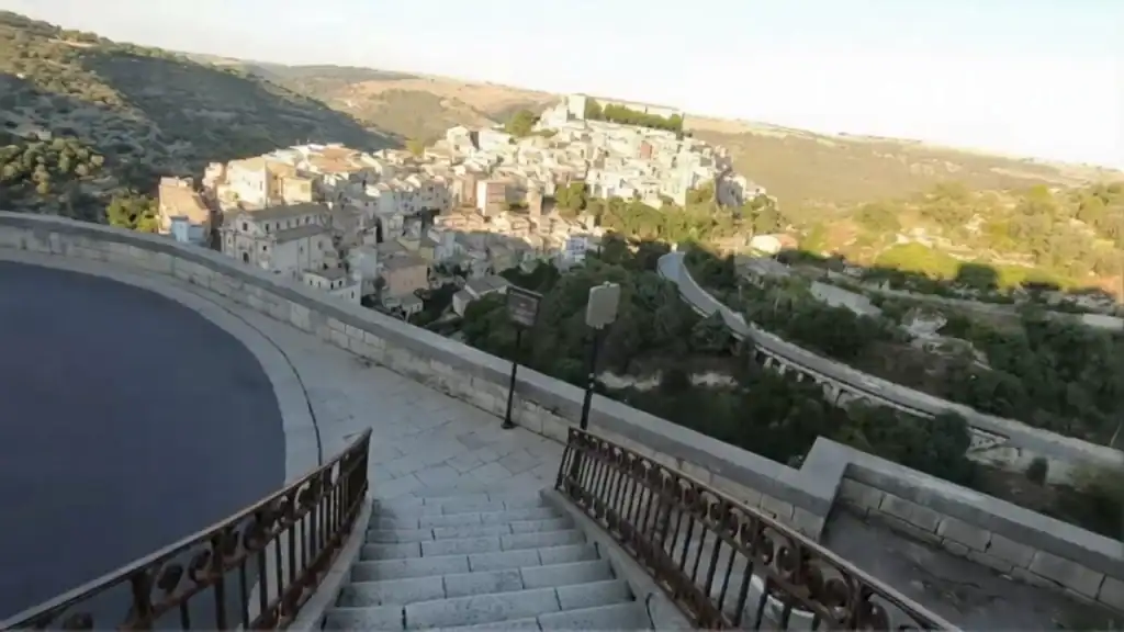 Stone staircase descending Via Scale toward Ragusa Ibla in Sicily, iron railings on both sides and the old town clustered on its ridge below