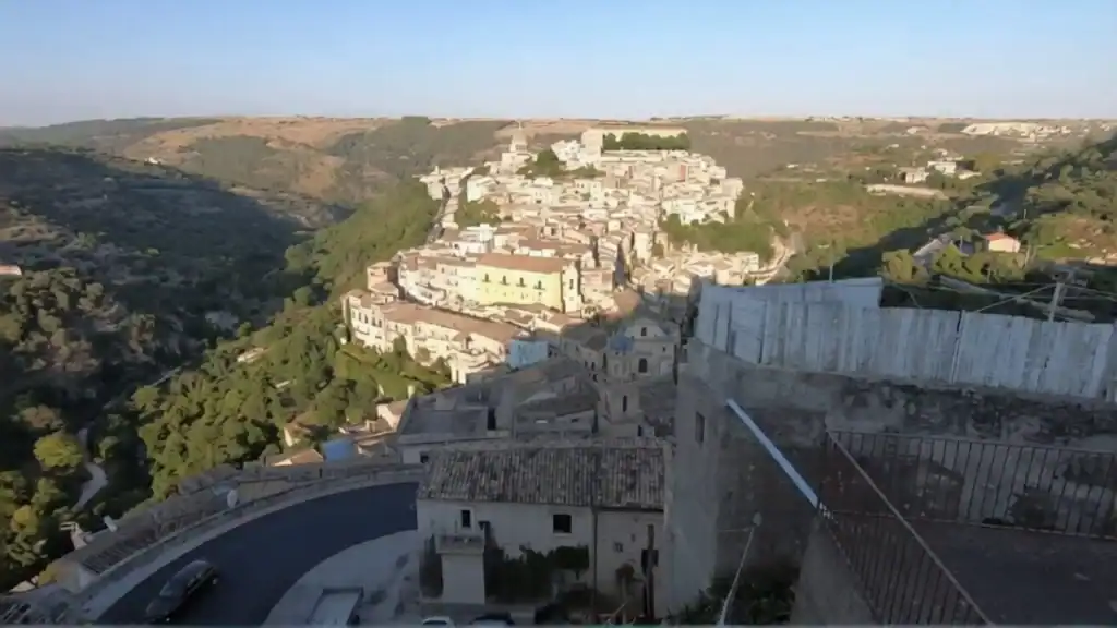Ragusa Ibla spreading across a limestone ridge in Sicily, flanked by wooded ravines, with the dome of San Giorgio visible at its crest