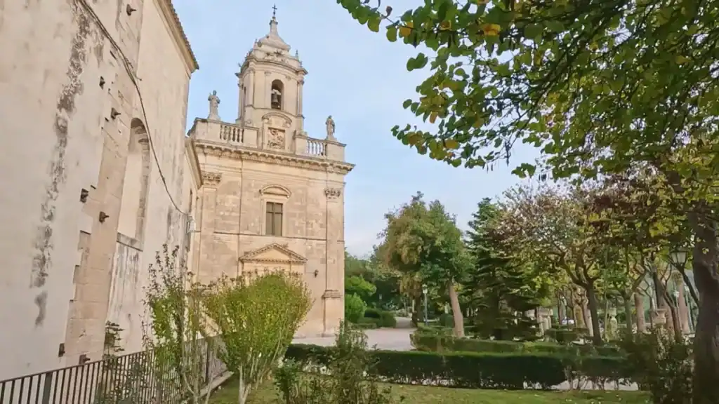 Santa Maria delle Scale's ornate limestone tower seen from within Villa Margherita, stone saints on the balustrade visible against an open sky