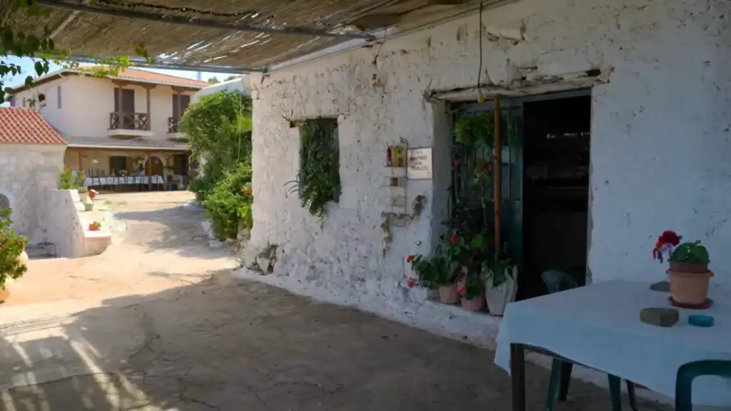 Whitewashed courtyard building at the Monastery of Agios Nikolaos Ieras on Lefkada island, potted flowers beside a doorway marked with a handmade local products sign.