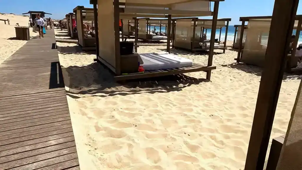 Rows of private cabanas with white mattresses lining a wooden boardwalk on pale sand