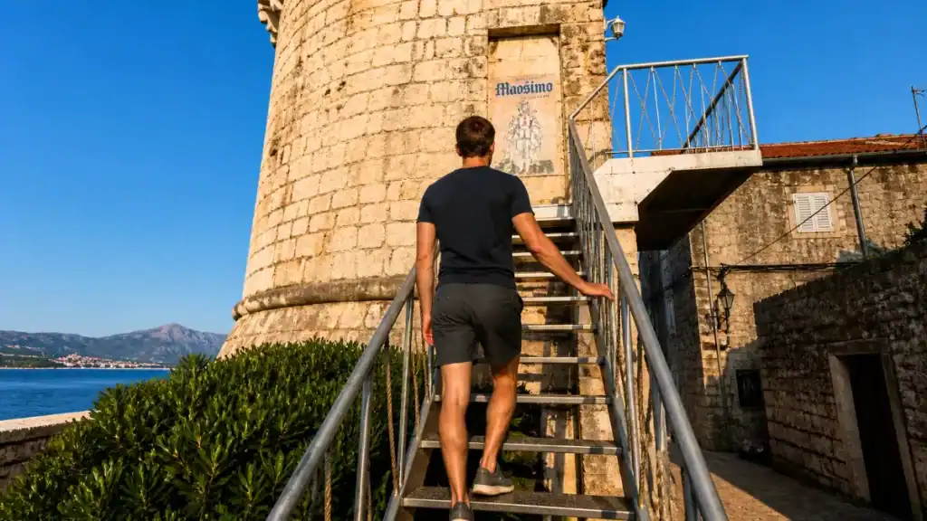 Man climbing metal staircase to Massimo cocktail bar inside Zakerjan Tower, Korčula