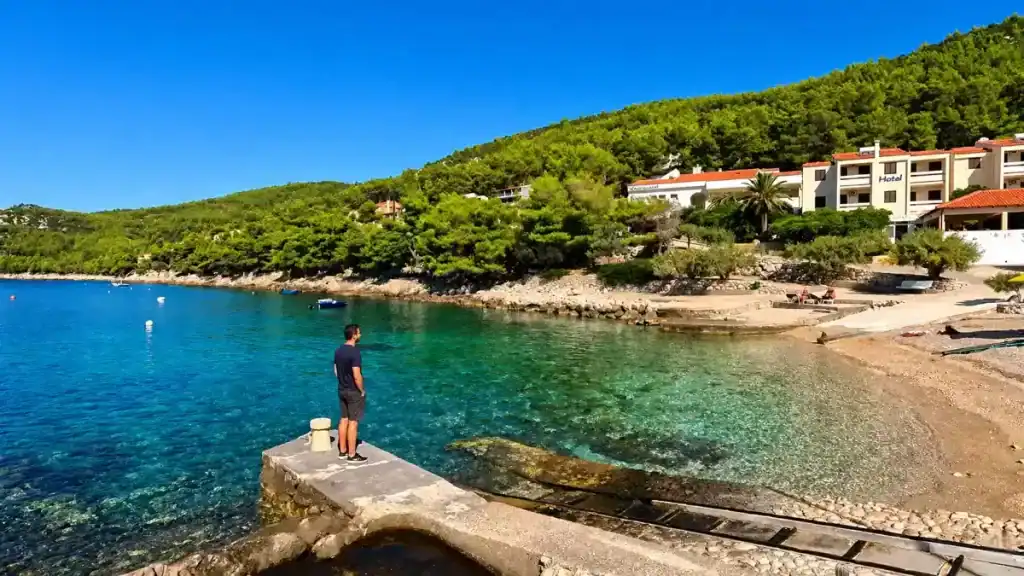 Man standing on a stone jetty overlooking the sheltered cove and pebble shore at Priscapac Beach, Korčula island